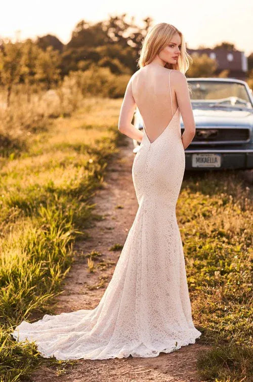 Woman in a white lace dress with an open back walking on a dirt path in a field.