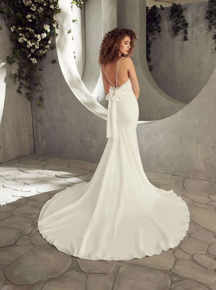 Woman in a white wedding dress standing in a stone-walled room with decorative plants.