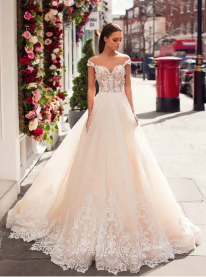 Woman in a white lace wedding dress standing in front of a floral decorated building.