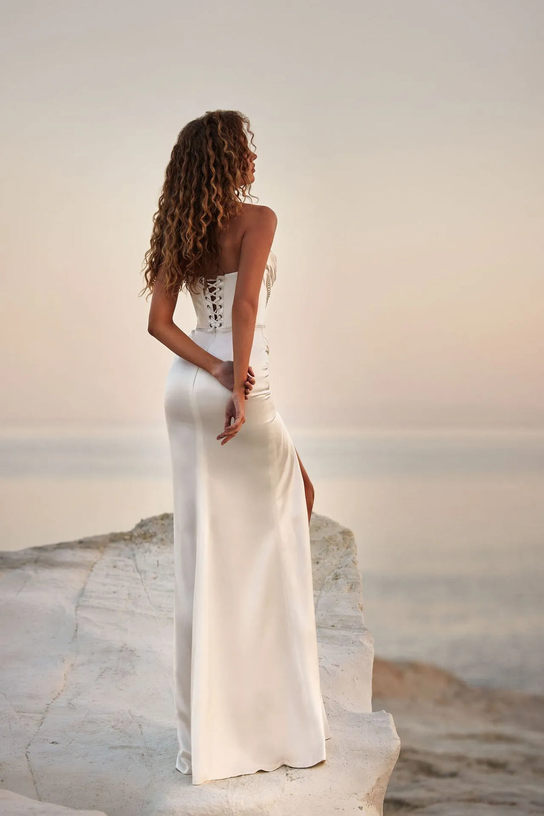 Woman in a white dress standing on a rocky beach with a sunset in the background