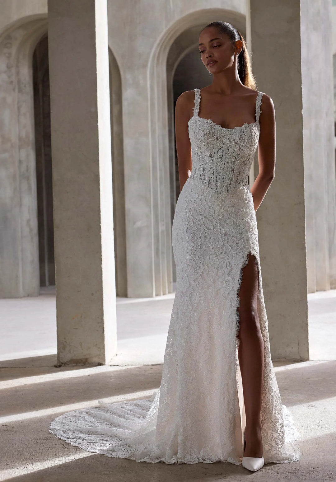 Woman wearing a white lace wedding dress with a high slit in an architectural setting.