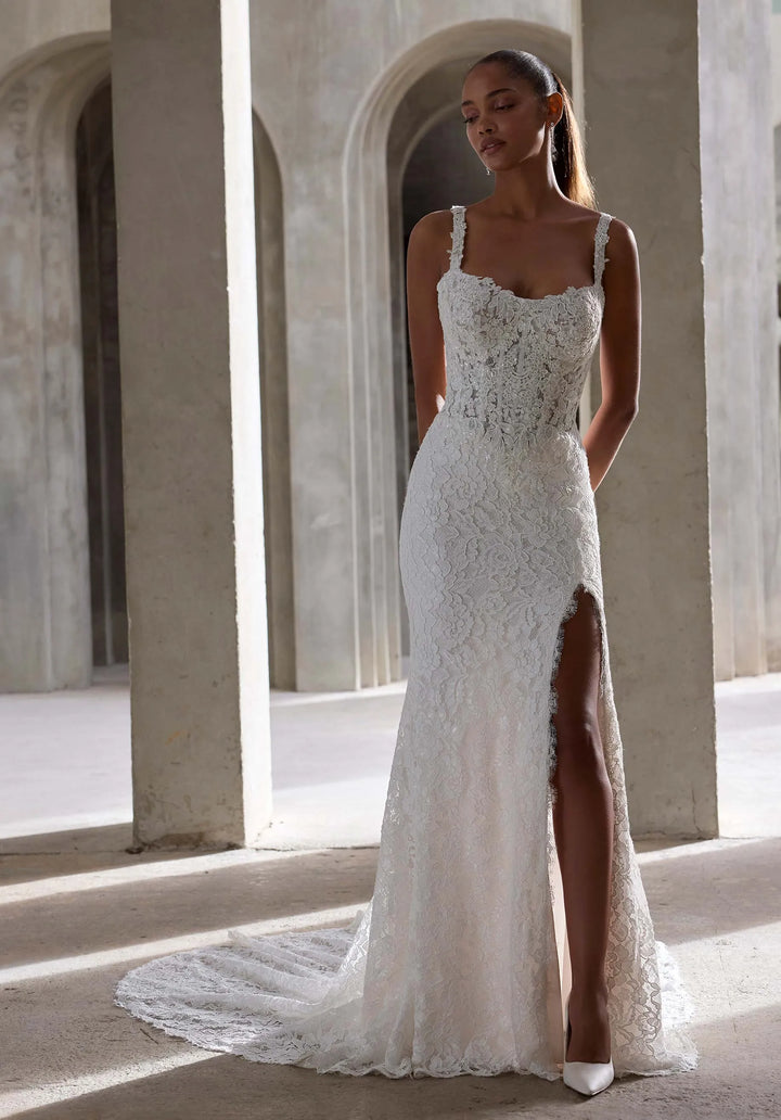 Woman wearing a white lace wedding dress with a high slit in an architectural setting.