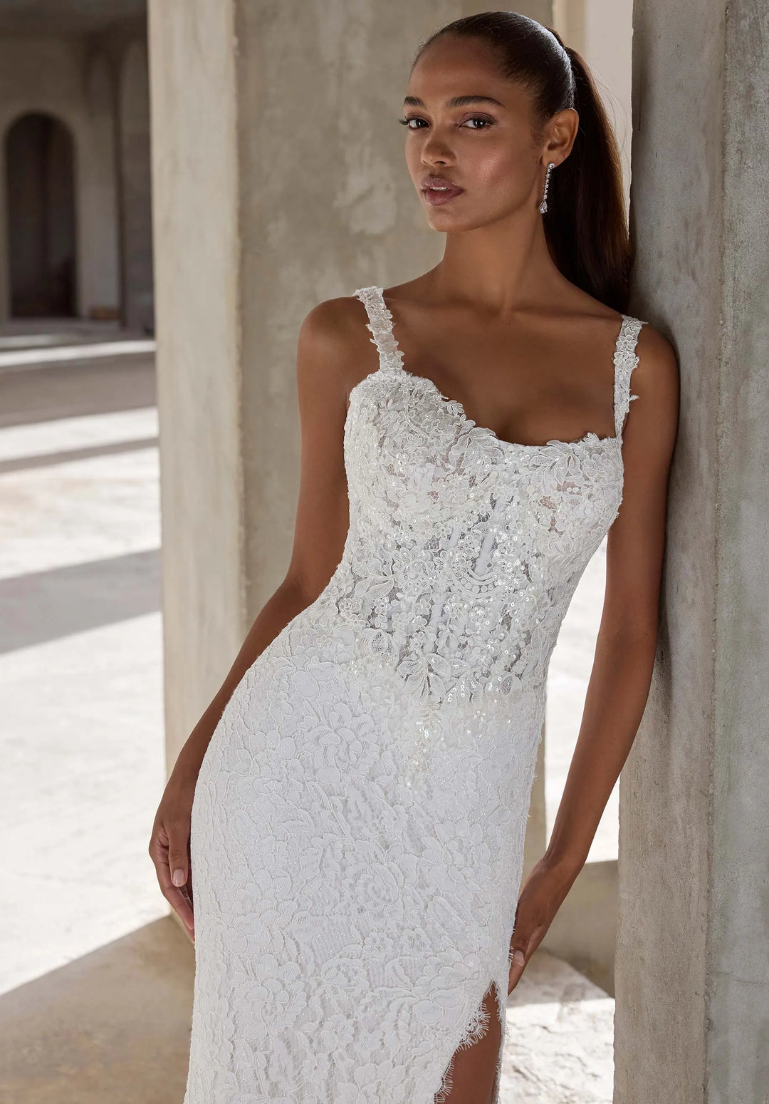 Woman wearing a white lace wedding dress standing against a stone wall.
