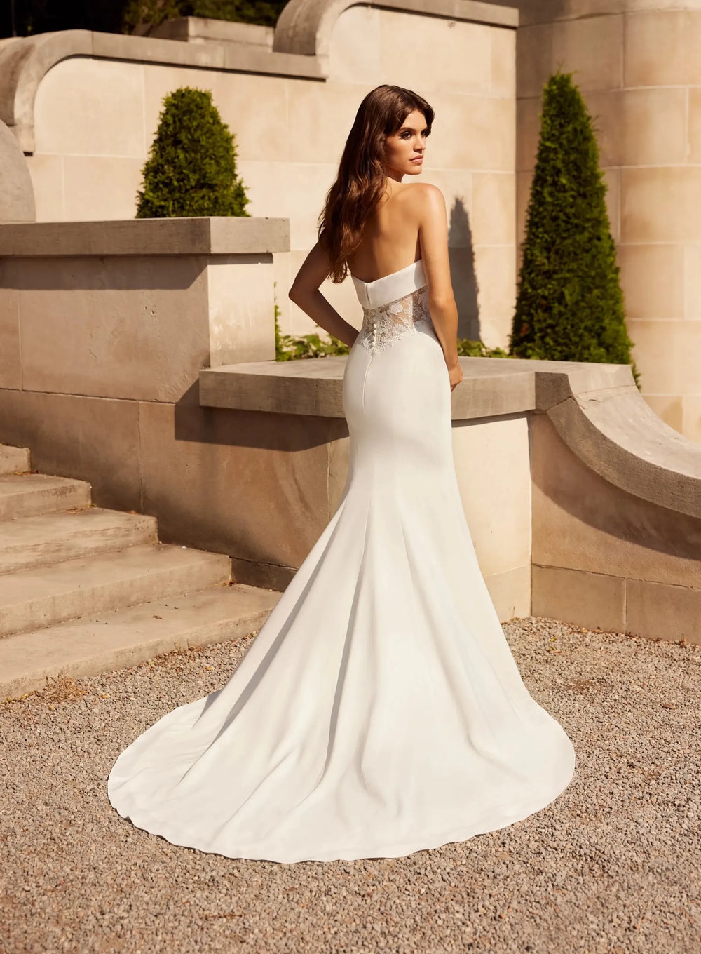 Woman in a white wedding dress standing in front of stone architecture.