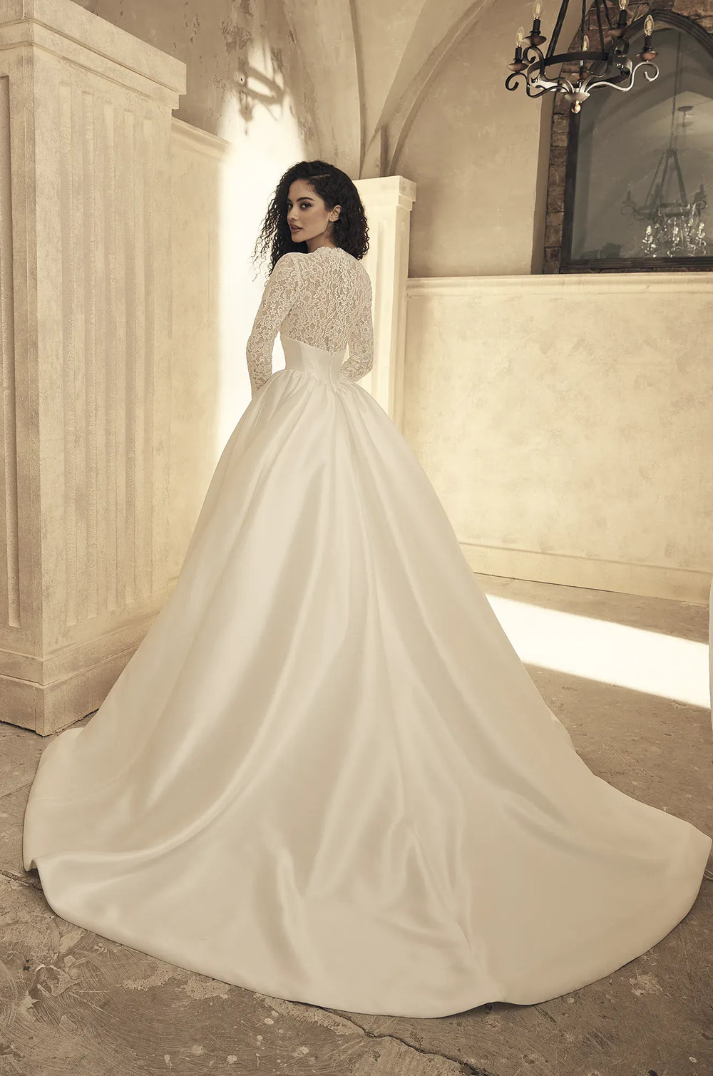 Woman in a white wedding dress standing in an elegant interior setting.