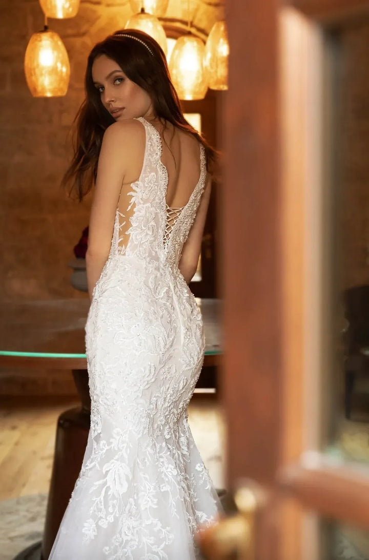 Woman in a white lace wedding dress standing in a warmly lit room.