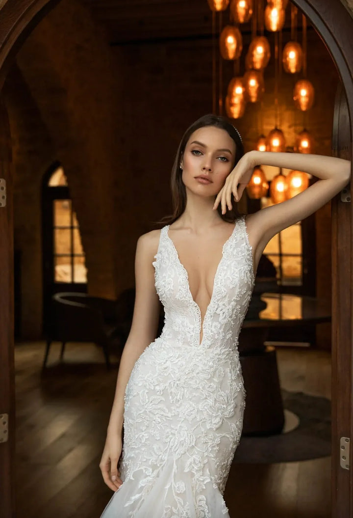 Woman in a white wedding dress standing in an elegant indoor setting with warm lighting.