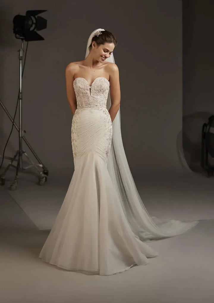 A strapless ivory wedding gown with a sweetheart neckline, lace-embellished bodice, and a long flowing train, shown on a model in a studio setting.
