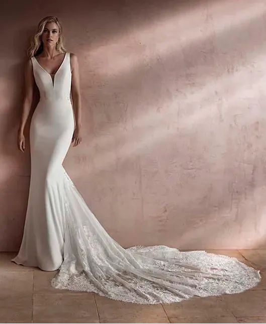 Woman in a white wedding dress with a long train standing against a textured wall.
