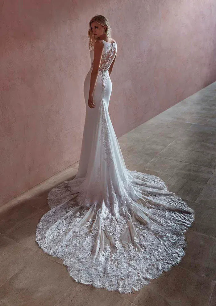 Woman wearing a white lace wedding dress with a long train in a softly lit room.