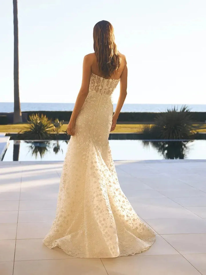 Woman in a strapless lace wedding dress standing by a pool with palm trees in the background