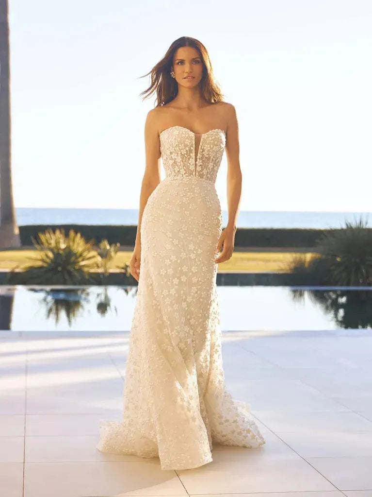 Woman in a strapless lace wedding dress standing by a pool with palm trees in the background