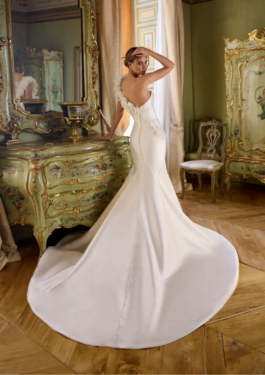 Woman in a white wedding dress standing in an ornate room with large mirrors and decorative furniture.