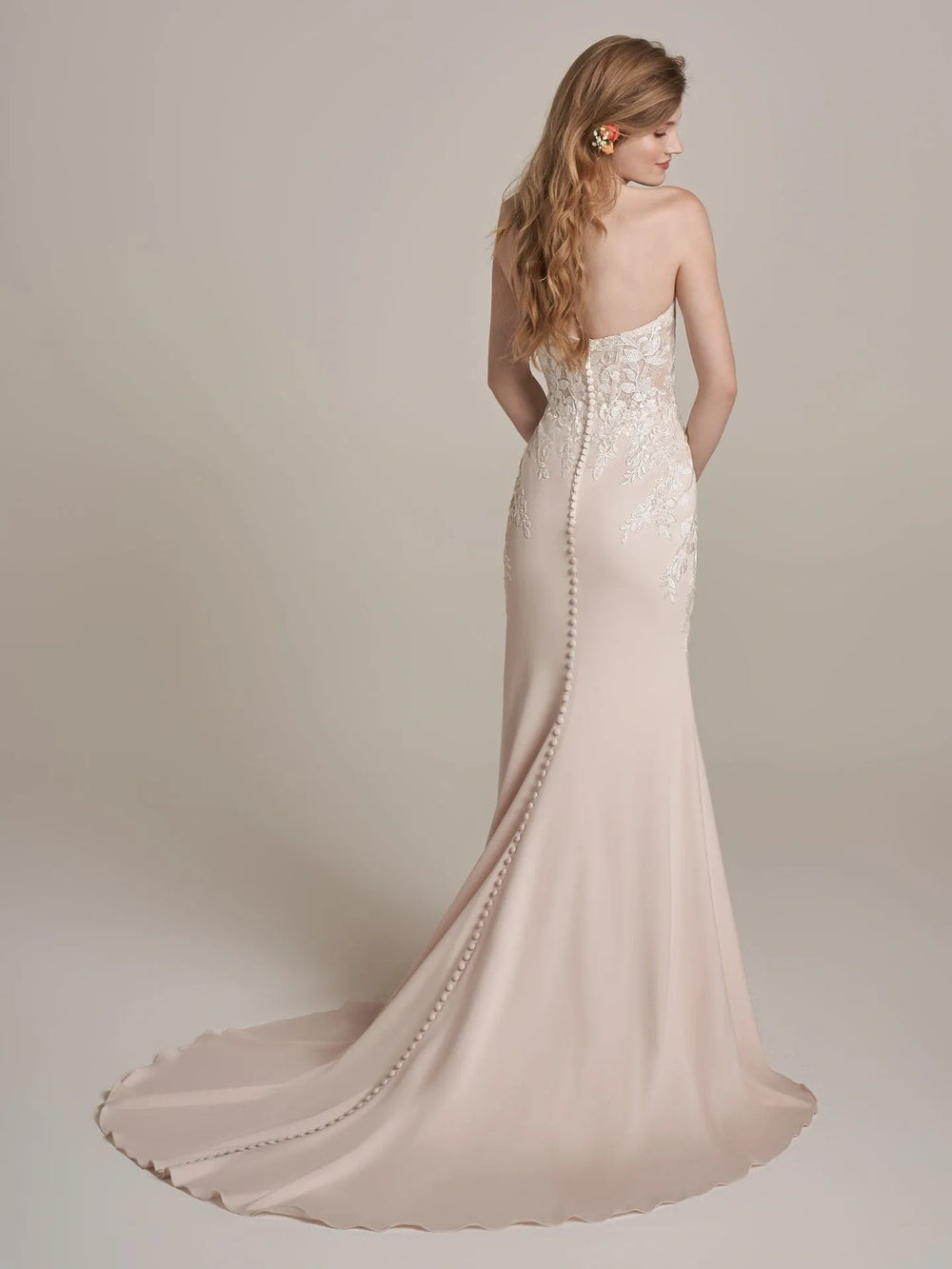 Woman wearing a strapless, embellished wedding dress with a long train on a plain background