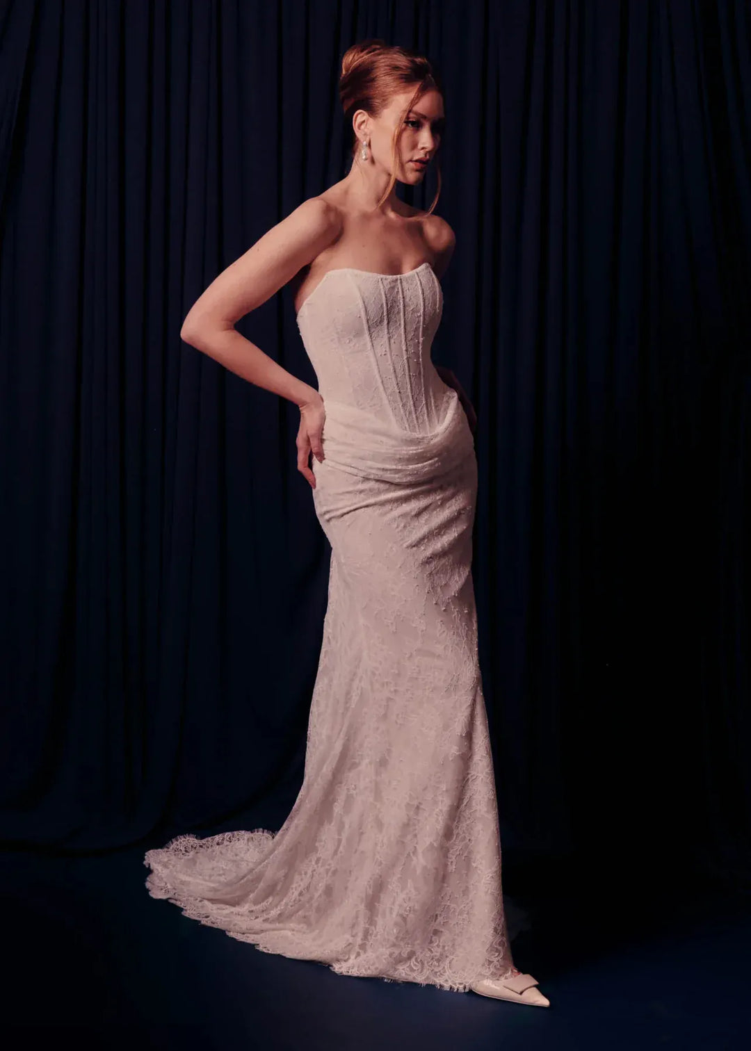 Woman wearing a strapless lace gown against a dark curtain background