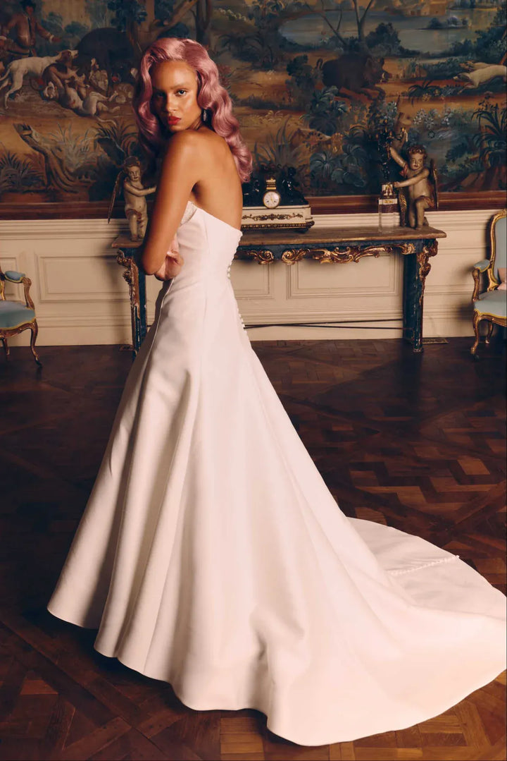 Woman in a white wedding dress standing in an ornate room with classical paintings.