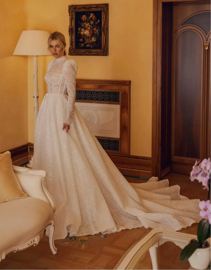 Woman in a white lace wedding dress standing in a room with yellow walls and decorative elements.