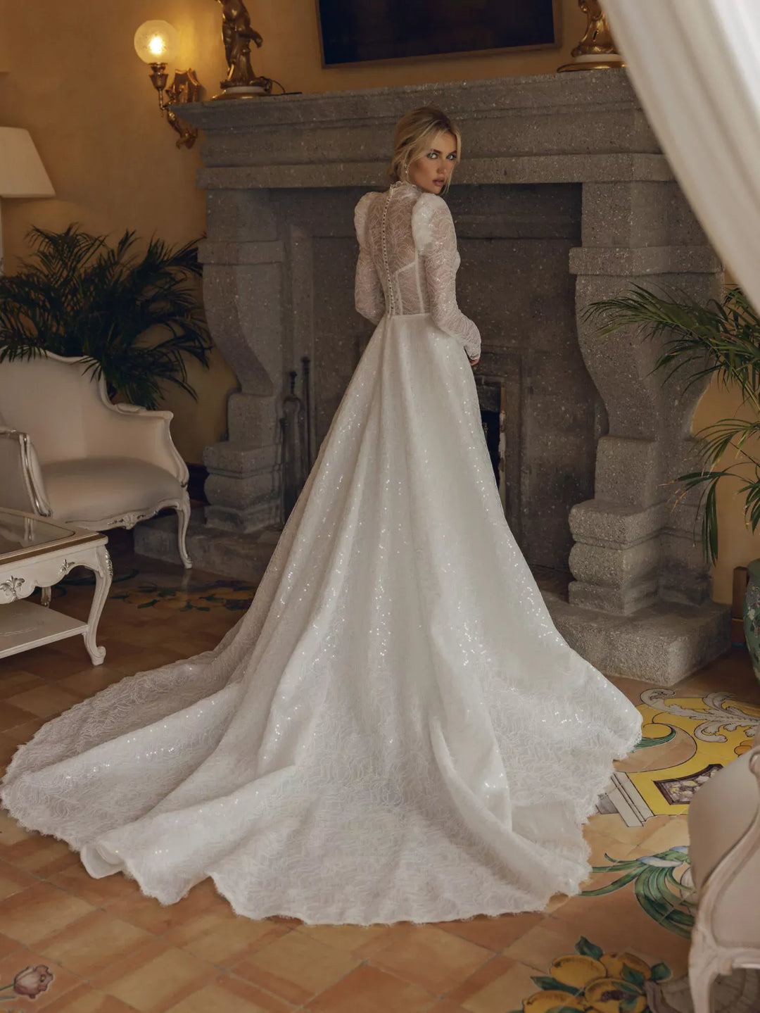 Woman in a white wedding dress standing in a room with a fireplace and decorative elements.