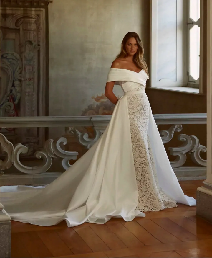 Woman in a white lace wedding dress standing in an elegant room with marble walls and a large window.