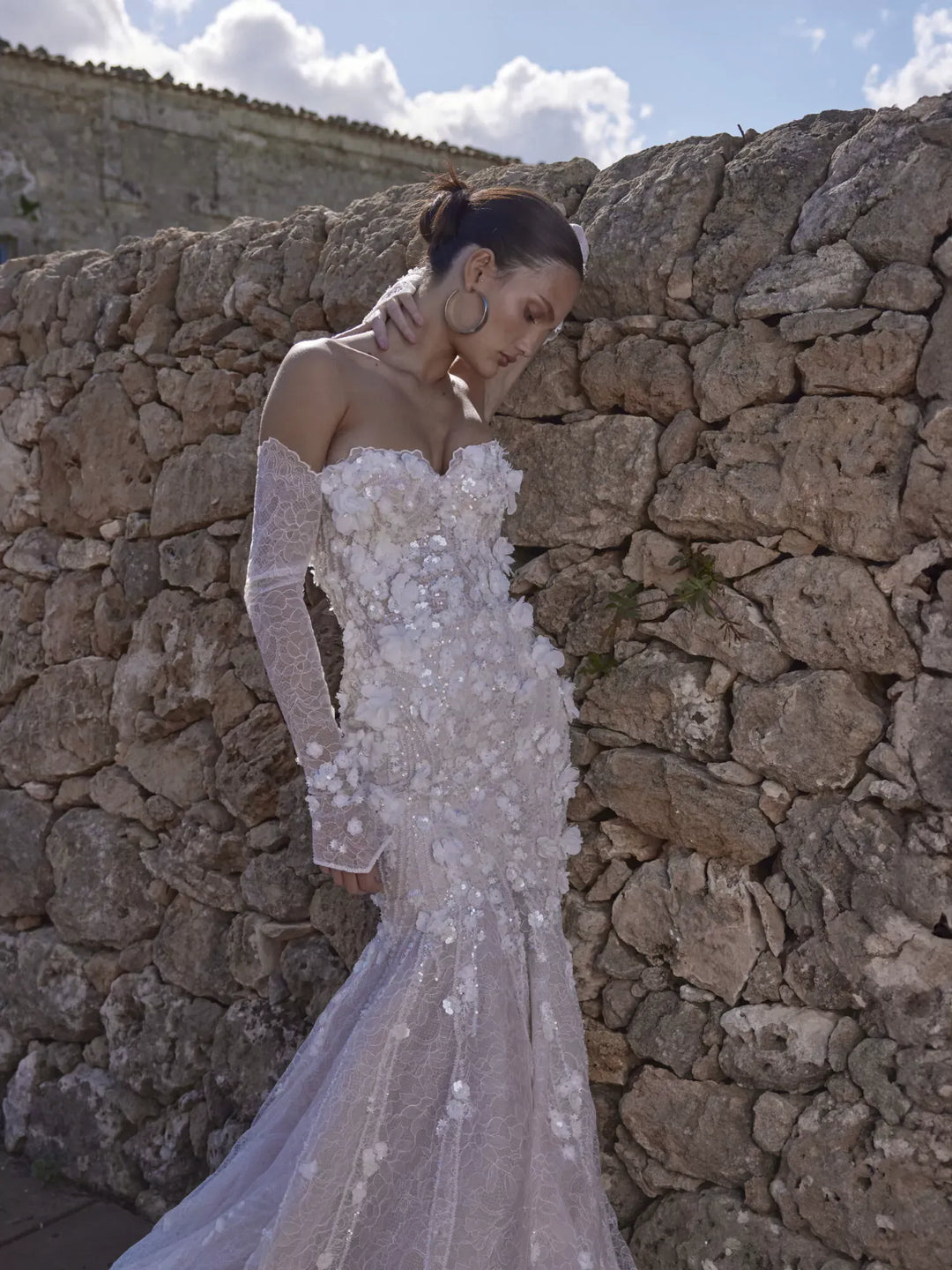 Woman in a white wedding dress standing against a stone wall.