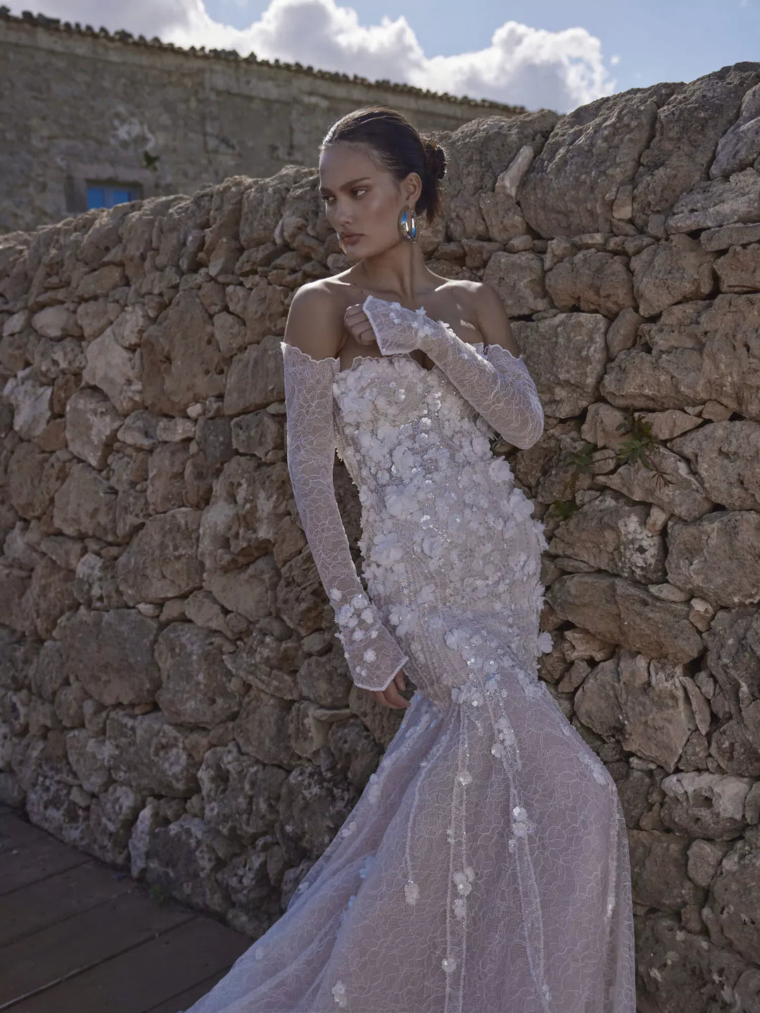 Woman in a white wedding dress standing against a stone wall.