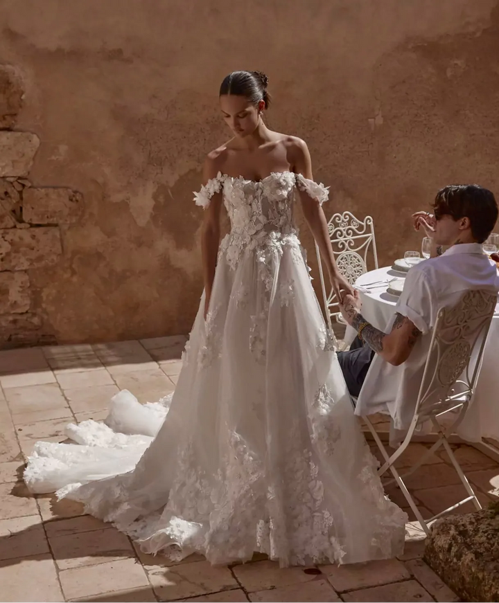 Woman in a white wedding dress standing outdoors near a stone wall.