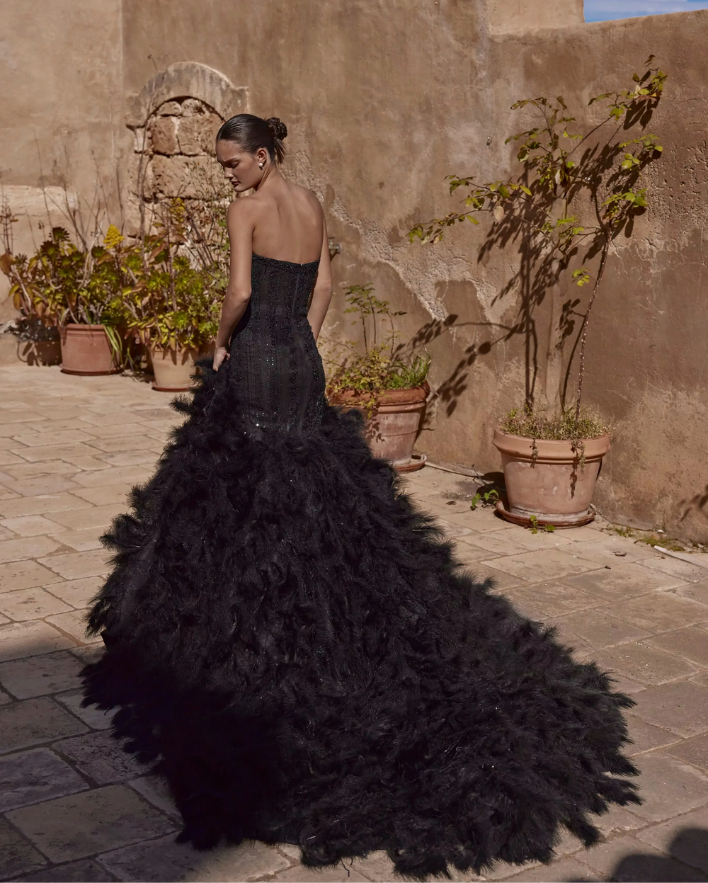 back of ricca sposa 25-013 black fit and flare wedding dress with a beaded strapless bodice and feathered skirt that extends into a long train