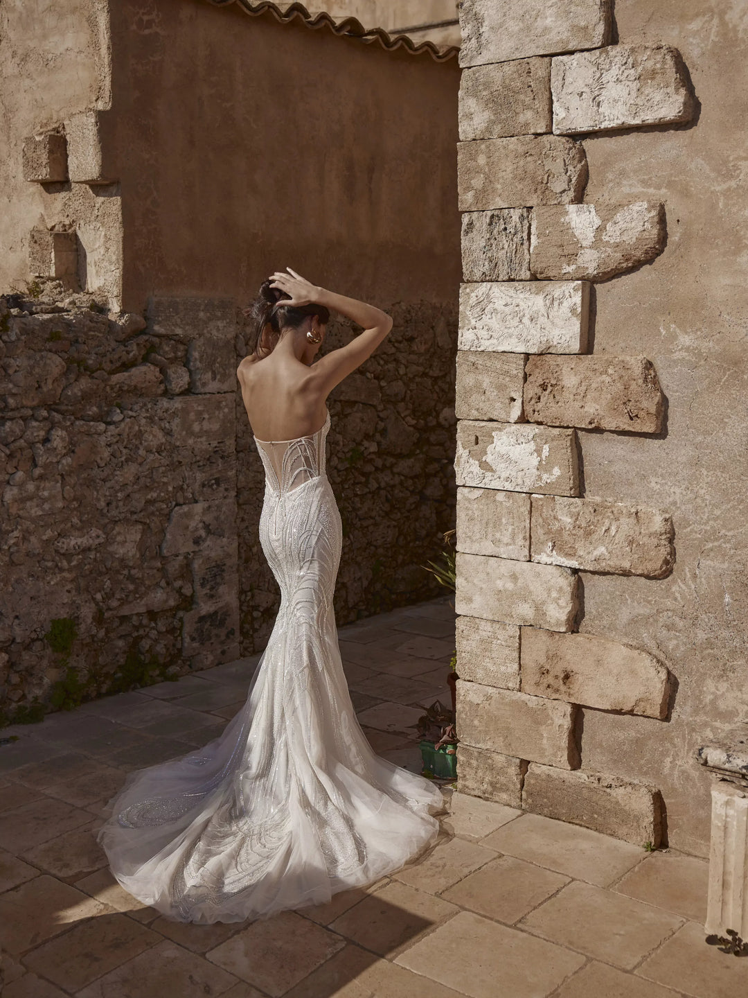 Woman in a white wedding dress standing in front of stone walls.