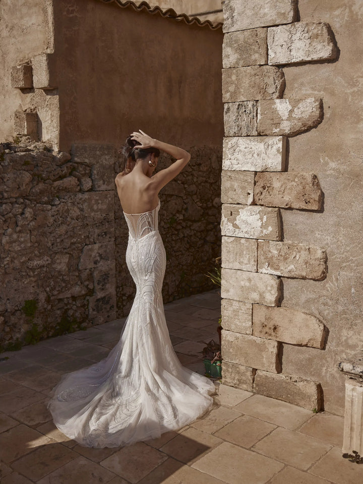 Woman in a white wedding dress standing in front of stone walls.
