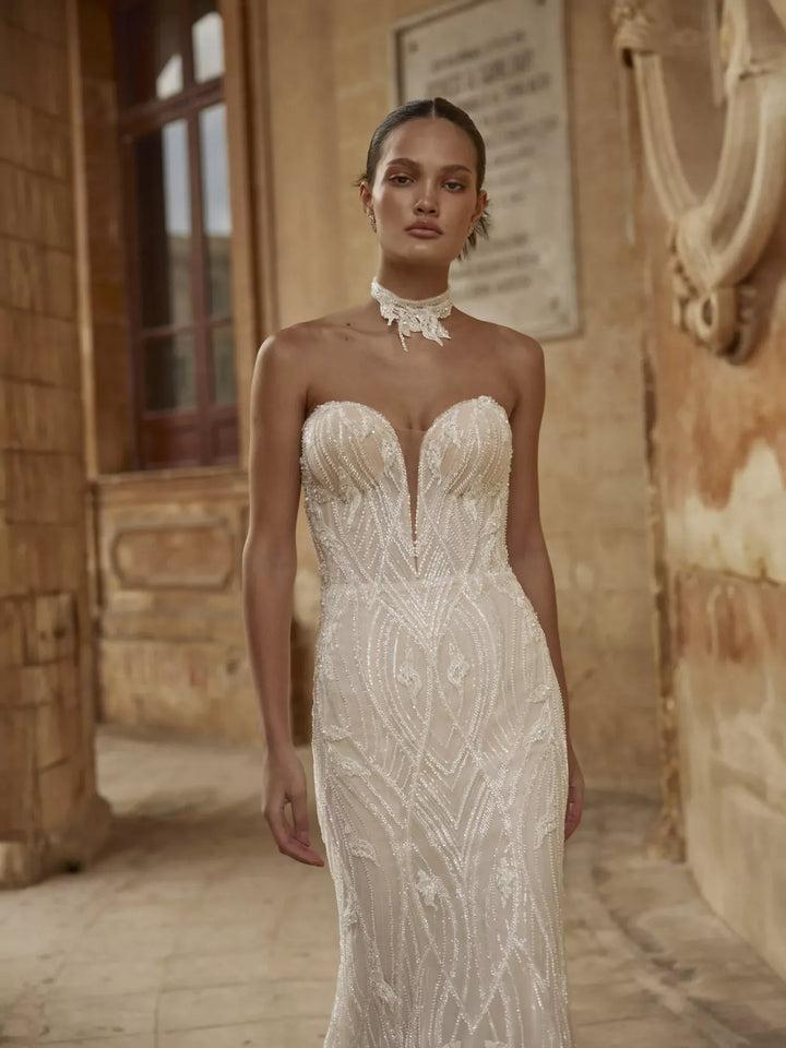 Woman wearing a strapless, intricately designed wedding dress in an outdoor setting.