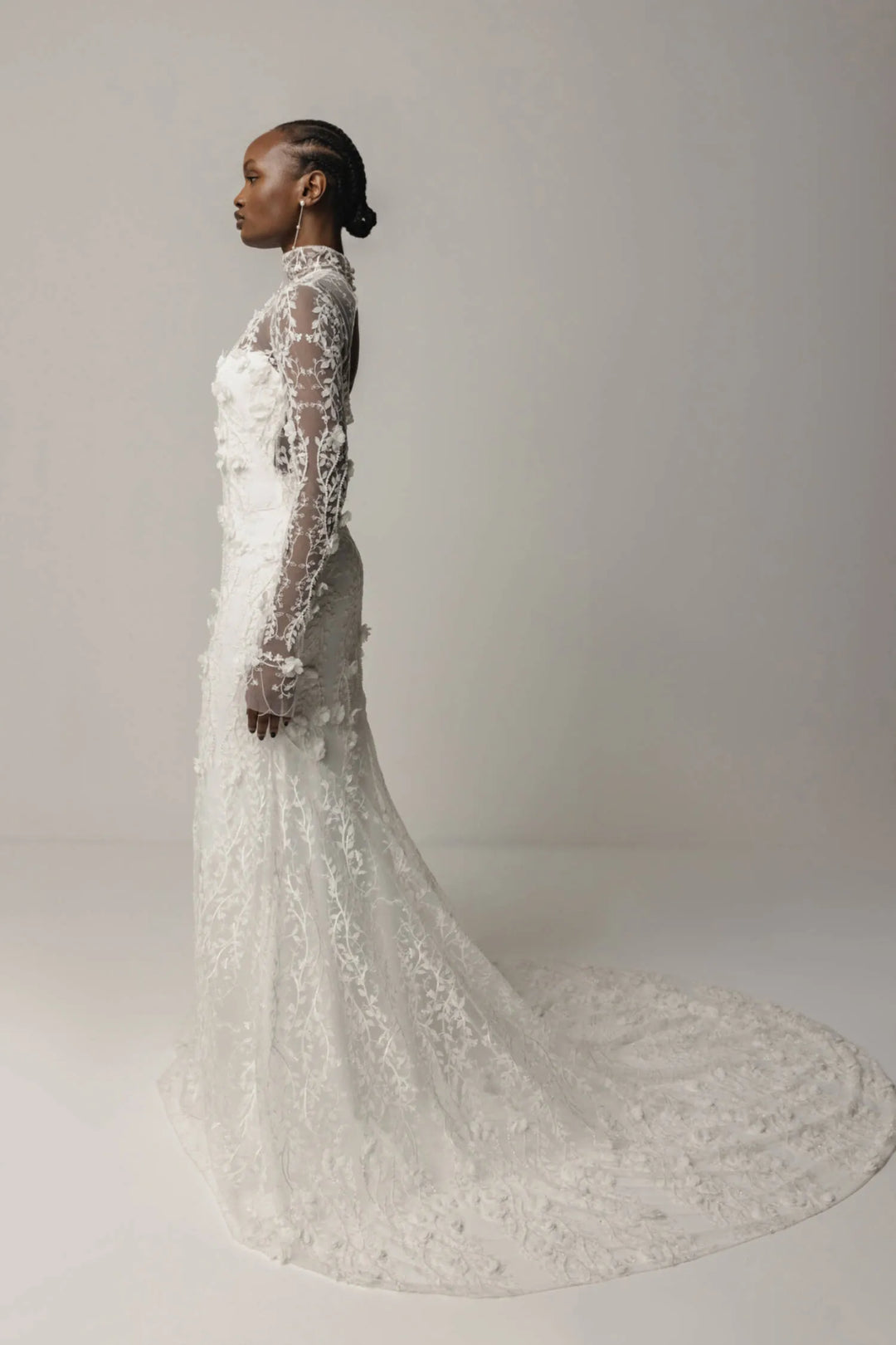 Woman wearing a long, elegant white lace dress against a plain background