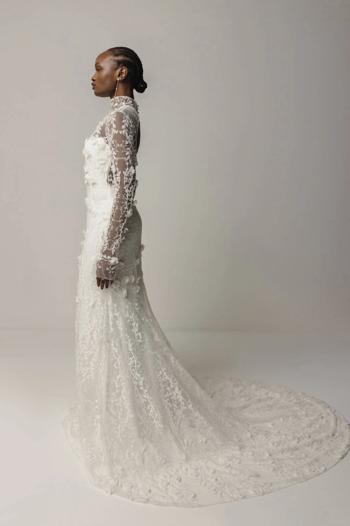 Woman wearing a long, elegant white lace dress against a plain background
