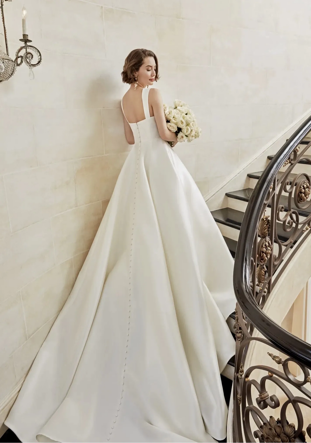 Woman in a white wedding dress standing on a staircase holding flowers.