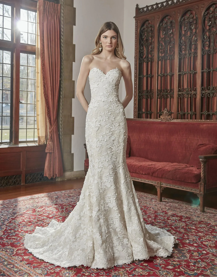 Woman in a strapless lace wedding dress standing in an elegant room with red curtains and a red sofa.