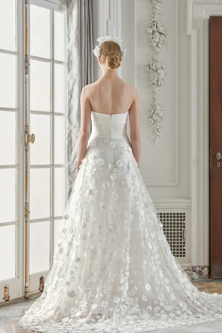 Woman in a white wedding dress standing in a room with large windows.