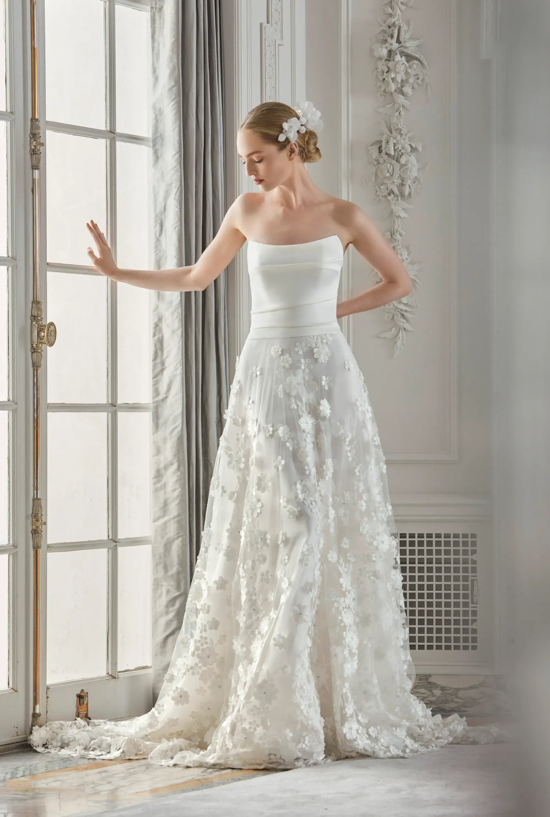 Woman in a white wedding dress standing in a room with large windows and decorative elements.