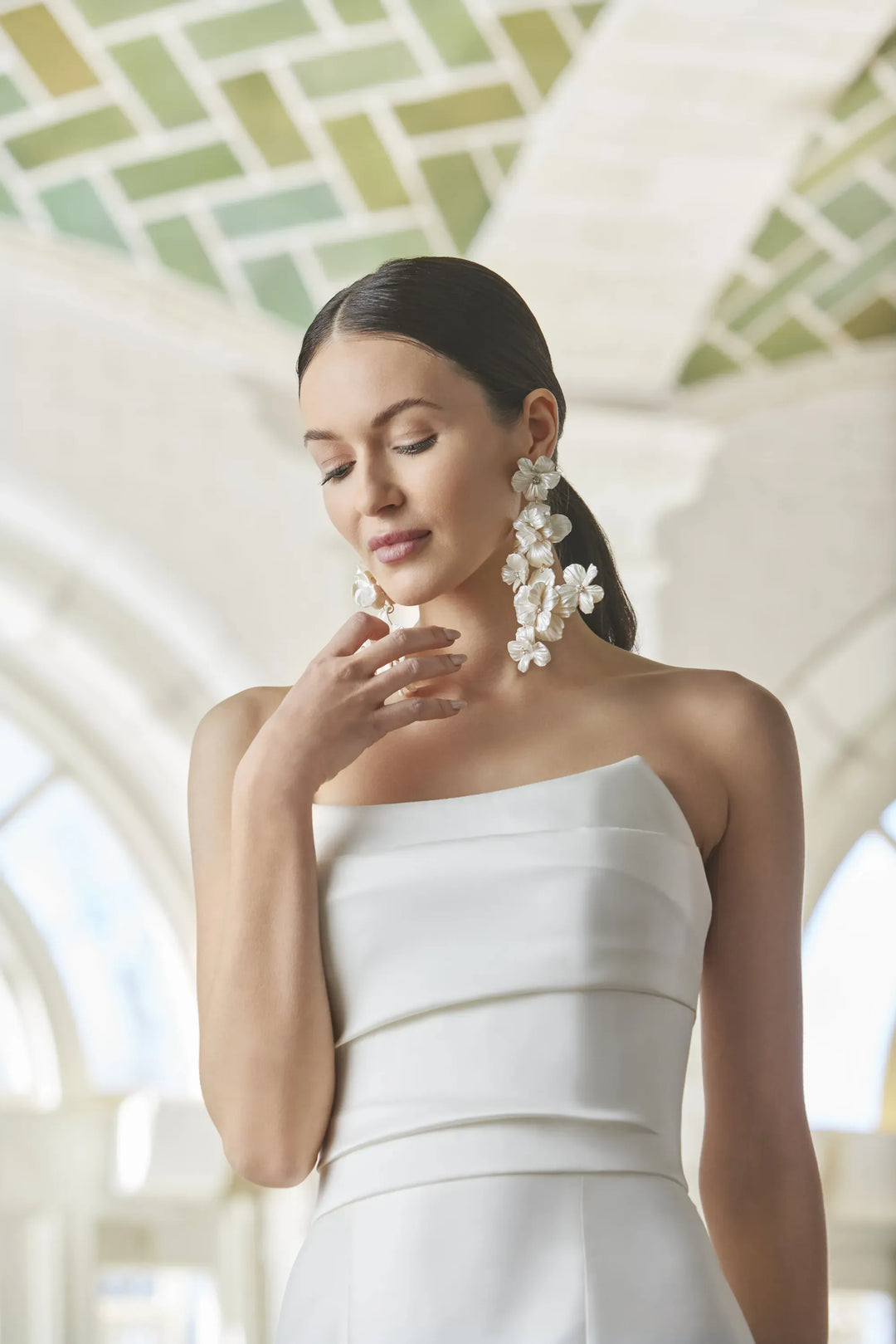 Woman in a white strapless dress with floral earrings in an elegant indoor setting