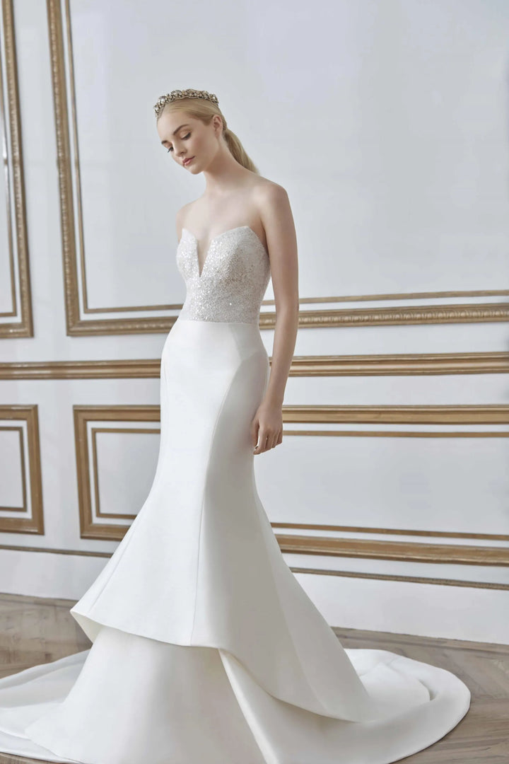 Woman wearing a strapless white wedding dress with a tiara against a decorative wall.