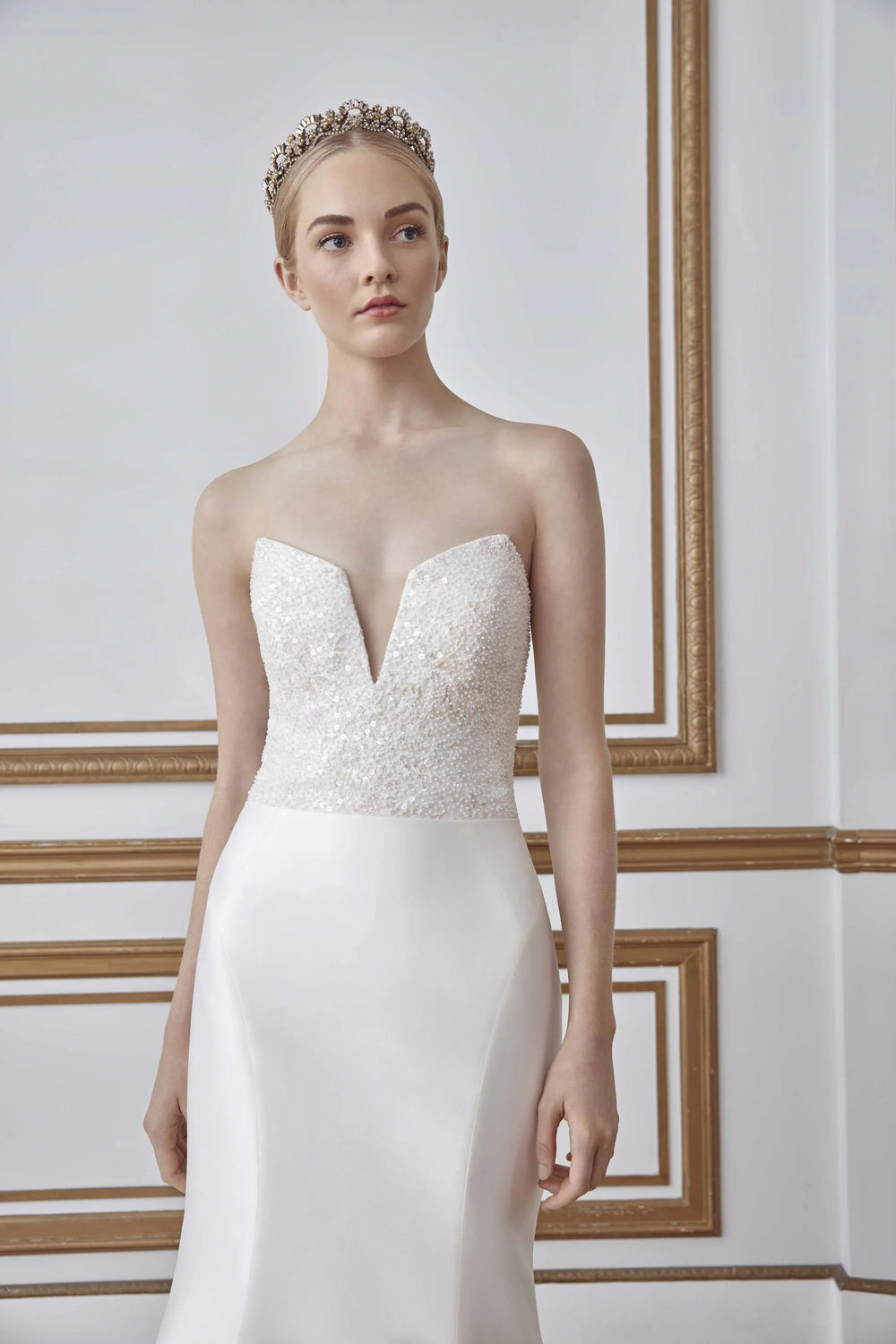 Woman wearing a strapless wedding dress with intricate detailing in an elegant room.