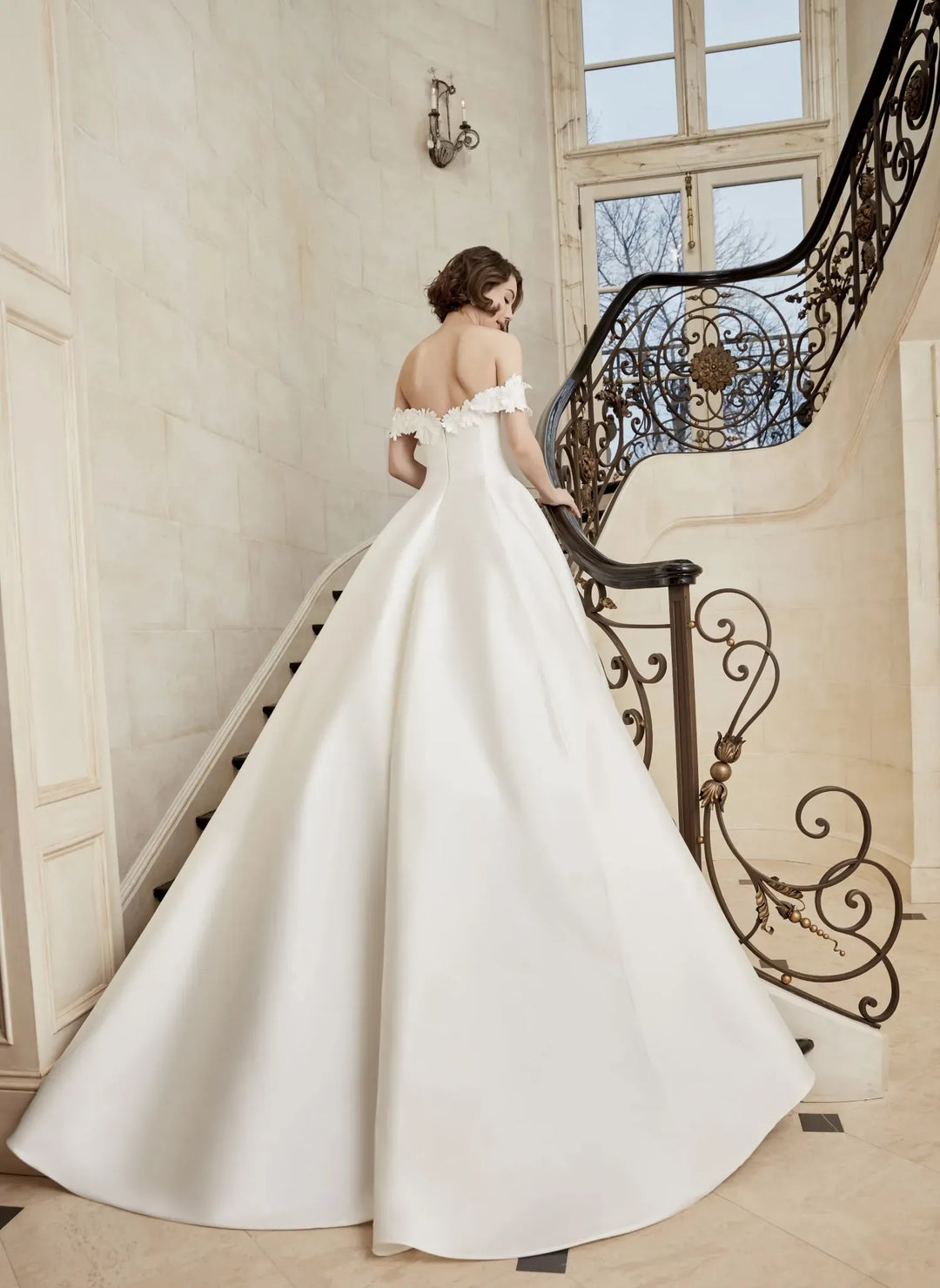 Woman in a white wedding dress standing on a staircase with ornate railings.