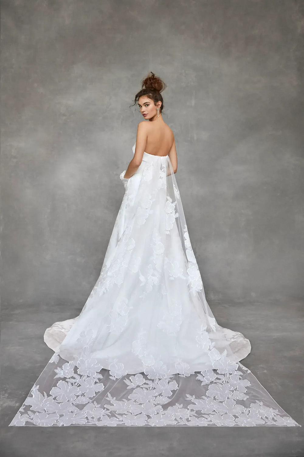 Woman in a white wedding dress with a long train against a gray background