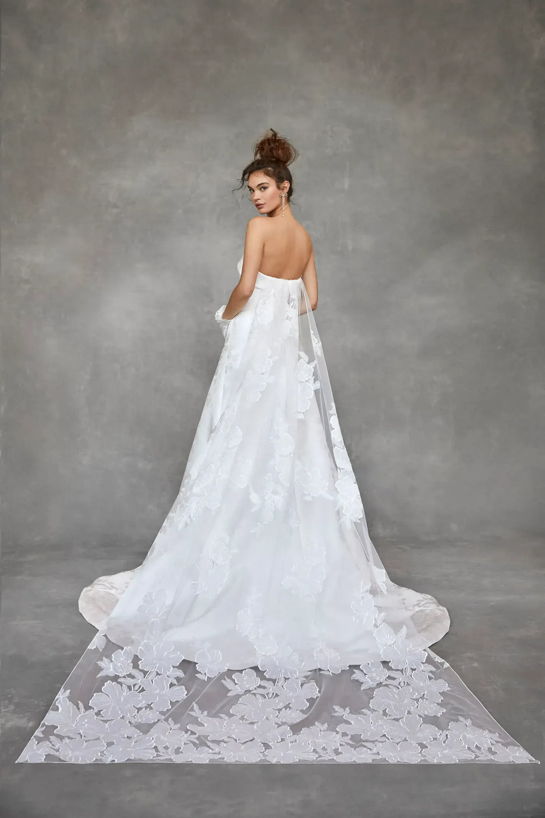 Woman in a white wedding dress with a long train against a gray background