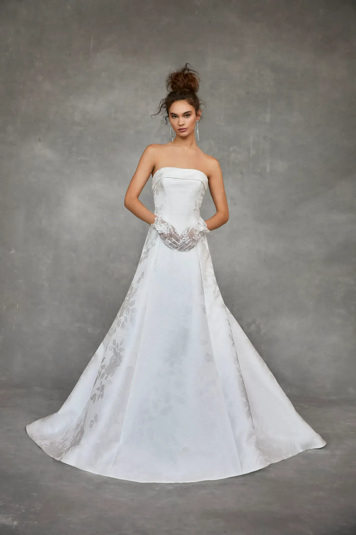Woman wearing a strapless wedding dress with lace details against a gray background