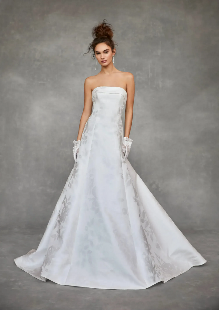 Woman wearing a strapless white wedding dress against a gray background