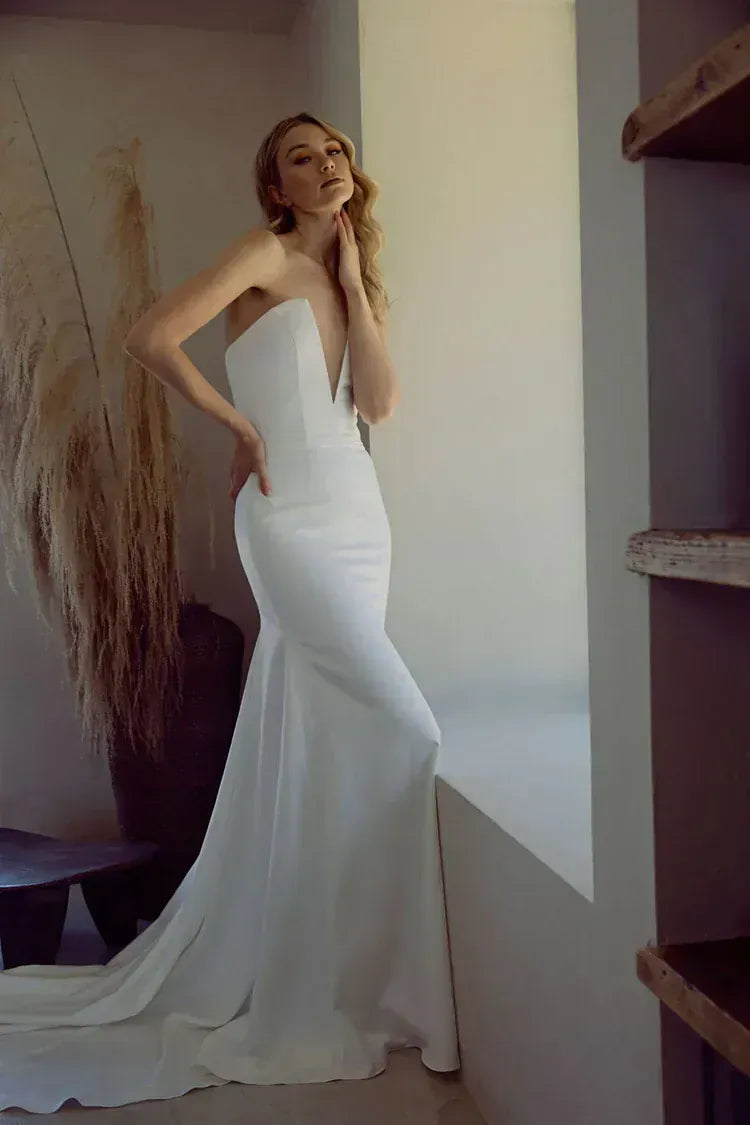 Woman in a white strapless gown standing in a minimalistic room.