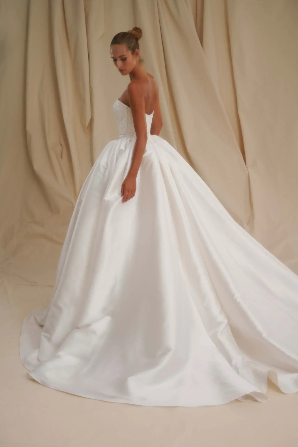 Woman wearing a white wedding dress against a beige curtain backdrop