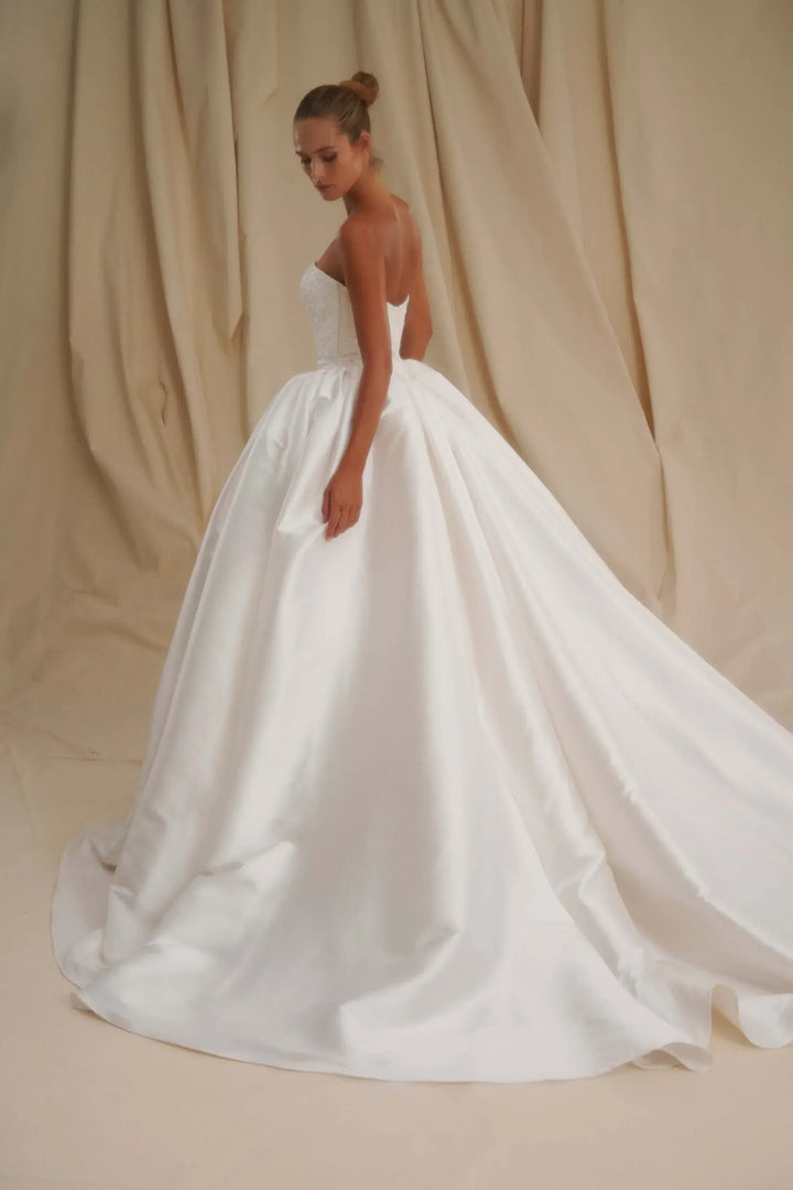 Woman wearing a white wedding dress against a beige curtain backdrop