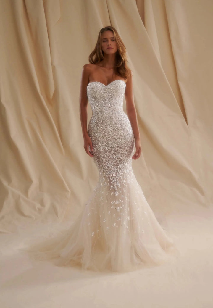 Woman wearing a strapless, beaded wedding dress against a beige curtain backdrop