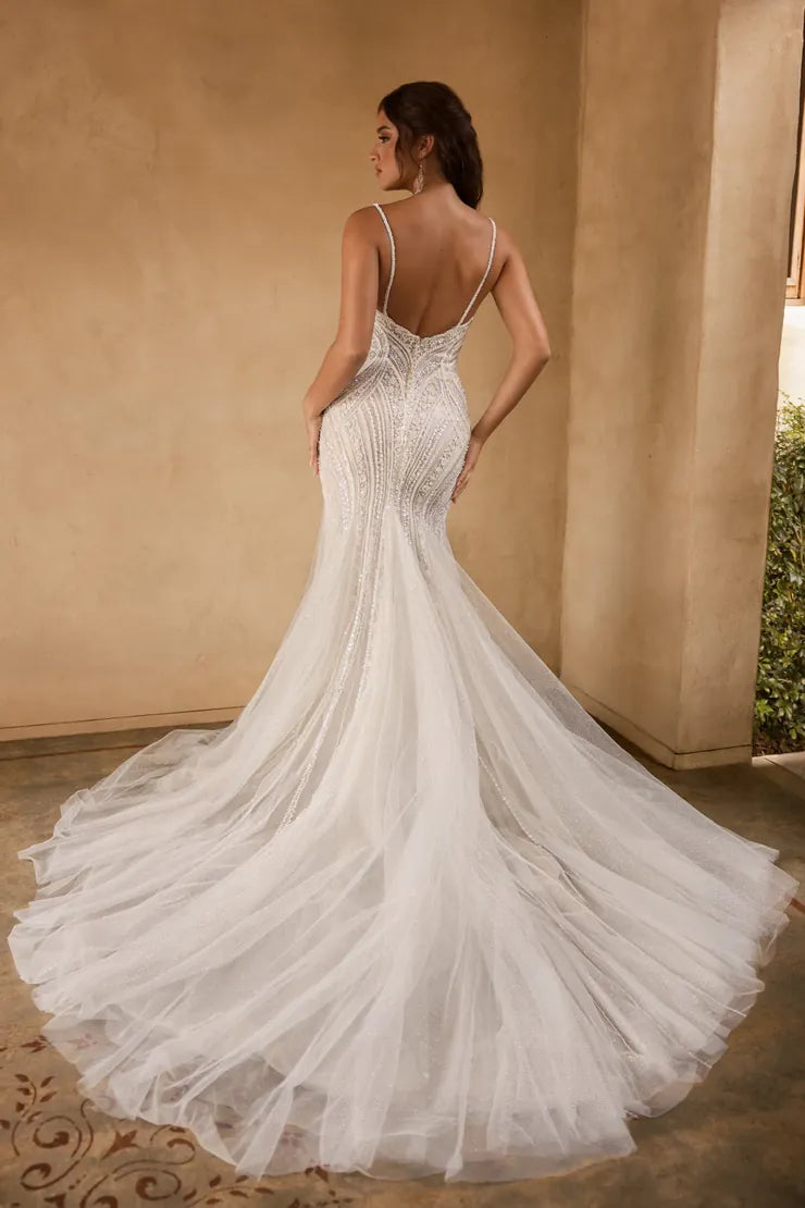 Woman in a white wedding dress with a long train, standing against a beige wall.