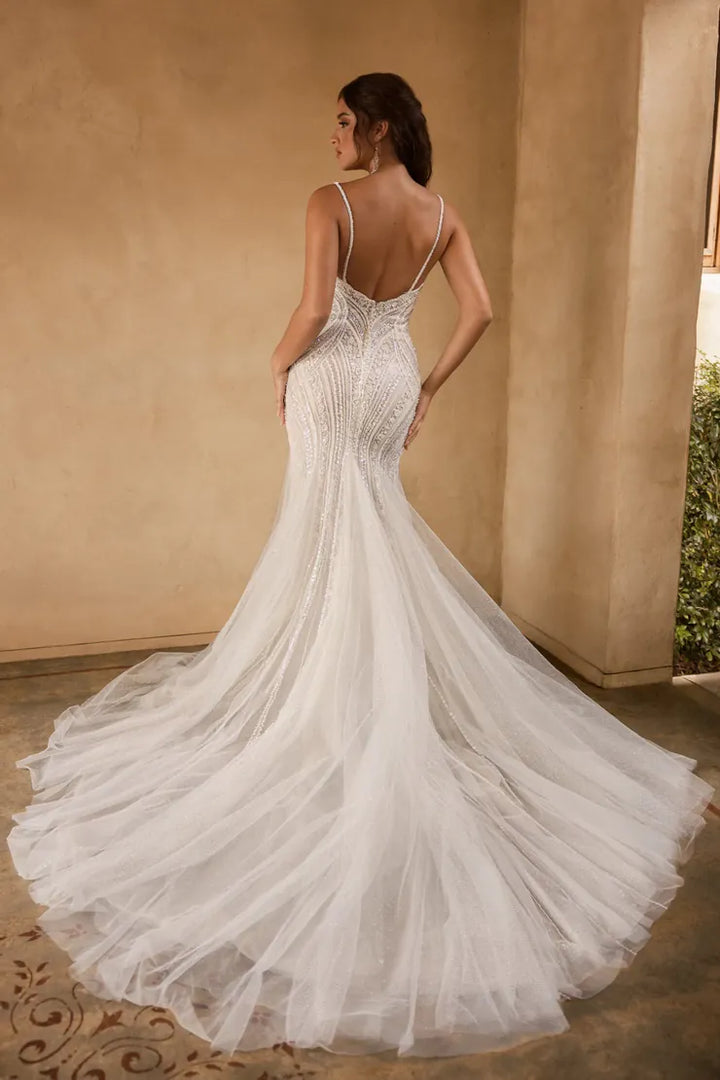 Woman in a white wedding dress with a long train, standing against a beige wall.